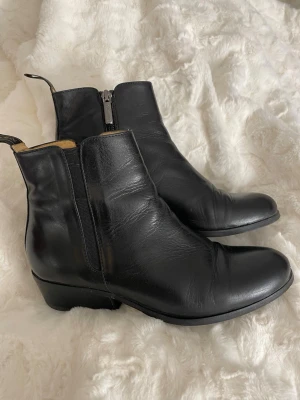 Svarta Chelsea boots från Novita - Stilrena svarta Chelsea boots från Novita i skinn. Klassisk rund tå, låg klack och elastiska paneler på sidorna för enkel påtagning. Boots med dragflikar och dragkedja på insidan. Perfekta för dig som gillar tidlös och clean stil.