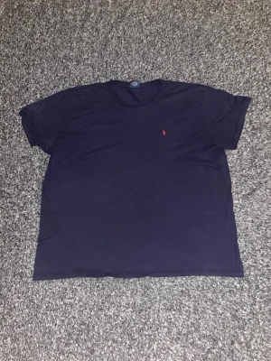 Mörkblå t-shirt från Ralph Lauren - Klassisk mörkblå t-shirt från Ralph Lauren med rund halsringning och korta ärmar. Liten röd broderad logga på bröstet ger en clean och stilren look. Tillverkad i mjuk bomull för maximal komfort. Detta är en väldigt stor tröja och passar dig som är lite större. Hör av dig vid intresse!😃