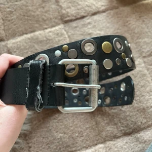 Svart nitbälte med metallringar - Säljer ett svart bälte i konstläder med massor av silver- och guldfärgade nitar och stora metallringar
