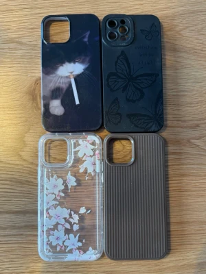  iPhone skal  - Fyra mobilskal till iphone 12 pro: ett svart med kattmotiv, ett svart med fjärilar, ett transparent med vita blommor och ett brunt ribbat skal. De är in princip oanvända. 