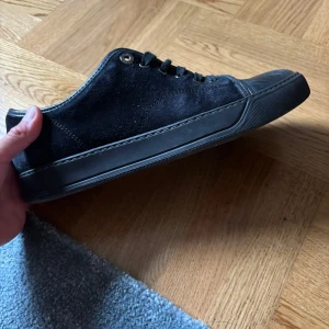 Lanvins skor - Stilrena svarta sneakers i mocka med matchande svart sula och snörning. Skorna har rund tå och metallöglor för snören, samt diskreta sömmar som ger en clean look. Perfekta för dig som gillar en enkel men snygg stil.