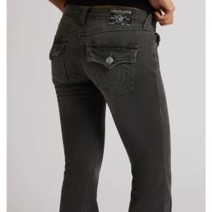 Grå bootcut jeans från True Religion - Snygga grå jeans från True Religion med bootcut passform och dekorativa ficklock bak. Klassisk femficksmodell med silverfärgade knappar och detaljerad söm. Perfekta för dig som vill ha en cool och avslappnad look.