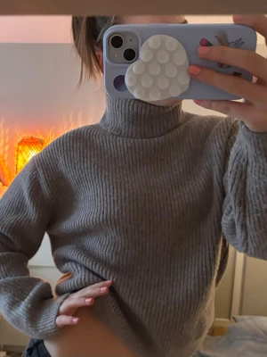 Grå ribbstickad polotröja - Mysig grå ribbstickad polotröja med hög krage och långa ärmar. Tröjan har en avslappnad passform och är perfekt för kalla dagar. Materialet känns mjukt och stretchigt, vilket gör den skön att bära.