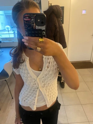 Vit virkad kortärmad kofta, helt oanvänd. Lappen kvar! - Söt vit virkad kofta med korta ärmar och v-ringning. Koftan har ett öppet mönster och knäpps framtill med två knappar. Perfekt att bära över ett linne för en trendig lager-på-lager-look.