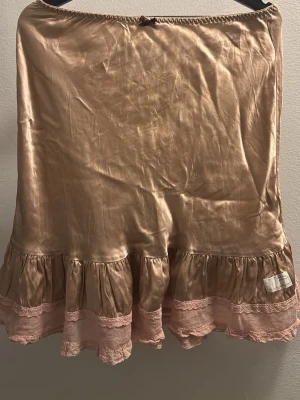 Champagnefärgad volangkjol i siden Odd Molly strl 2 - Supersöt kjol i champagnefärgat siden med volangkant och spetsdetaljer i ljusrosa. Kan användas både som kjol och underkjol. Superfint skick.