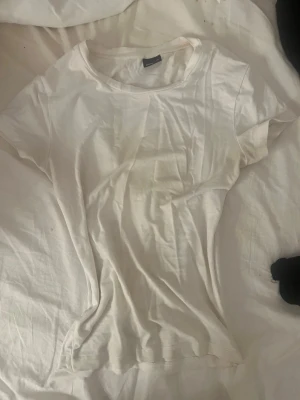 Vit basic t-shirt i bomull - En enkel vit t-shirt med rund hals och korta ärmar. Tillverkad i mjuk bomull och har en klassisk passform som funkar till det mesta. Perfekt basplagg för garderoben. Behöver uppenbarligen tvättas för den har smink fläckar men jag fixat det om nån köper