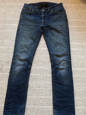 Mörkblå Nudie Jeans - Säljer ett par mörkblå skinny jeans från Nudie Jeans med klassisk femficksdesign och snygga slitningar på benen. Jeansen har en smal passform och är tillverkade i slitstarkt denim med kontrastsömmar och broderade bakfickor.30/32💯Har lagat med snyggt sashiko mönster