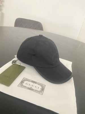 Gucci svart GG Keps - Snygg svart keps från Gucci med klassisk böjd skärm och diskret logga. Kepsen är tillverkad i ett slitstarkt tyg och har en stilren design som passar till många outfits. Perfekt accessoar för dig som gillar exklusiva märken och enkel stil.