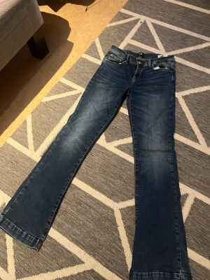 Blå bootcut jeans från LTB - Säljer ett par blå bootcut jeans från LTB med klassisk femficksdesign och snygga slitningar. Jeansen har normal passform och är tillverkade i ett mjukt bomullsmaterial med lite stretch för extra komfort. Perfekta för dig som gillar en tidlös jeanslook.