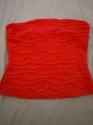 Röd bandeau tubtopp från SHEIN - Snygg röd bandeau tubtopp från SHEIN med vågig struktur i tyget. Toppen är axelbandslös och har en tight passform, perfekt för att skapa en trendig look. Enkel att matcha med både jeans och kjol.