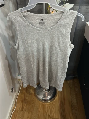 Grå ärmlös linnetopp från H&M - En enkel och stilren grå ärmlös linnetopp från H&M i ekologisk bomull. Perfekt för en avslappnad look och lätt att matcha med andra plagg. Rund halsringning och mjukt material som känns skönt mot huden.