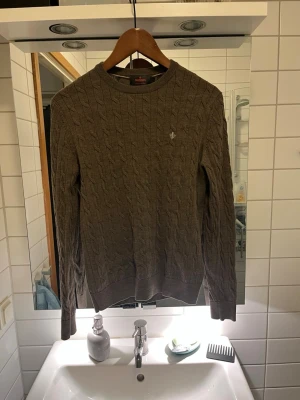 Brun kabelstickad tröja Morris - Säljer en brun kabelstickad tröja från Morris i 100% merinoull. Tröjan har rund halsringning, långa ärmar och en liten broderad logga på bröstet. Perfekt för dig som gillar klassisk och stilren design. Passar väldigt bra till både lite mer uppklätt men även skolan. Extremt bra skick.