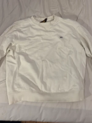 Vit sweatshirt från Lee - Klassisk vit sweatshirt från Lee i regular fit. Tröjan har rund halsringning, ribbade muddar vid ärmslut och nederkant samt diskret Lee-logga broderad på bröstet. Perfekt för en clean och enkel stil.