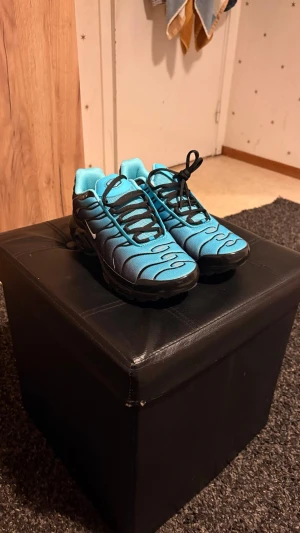 Blå Nike Air Max sneakers - Snygga blå Nike Air Max sneakers med svarta detaljer och snörning. Skorna har en sportig design med vågformade svarta linjer på ovandelen och en robust svart sula. Tillverkade i syntetmaterial och mesh för bra andningsförmåga.