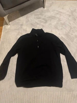 Svart halvzip tröja med hög krage - En stilren svart tröja med halv dragkedja och hög krage. Perfekt för lager på lager och enkel att matcha med olika outfits. Långa ärmar och mjukt material för en avslappnad look.