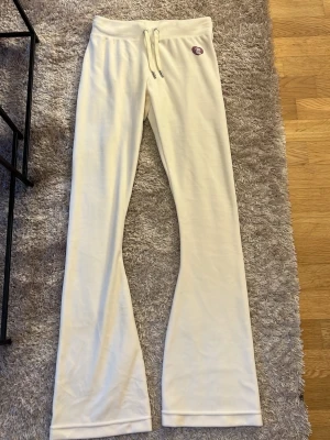 Vita mjukisbyxor med broderi - Snygga creme vita juicybyxor med snörning i midjan och detalj på baksidan. Byxorna har en rak och något utsvängd passform, perfekta för en snygg look. Mjukt material som känns skönt mot huden.