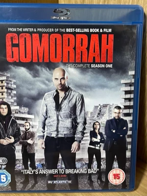 Gomorrah Säsong 1 Blu-ray - Blu-ray-box med hela första säsongen av den italienska kriminalserien Gomorrah. Serien är baserad på Roberto Savianos bok och utspelar sig i Neapel med fokus på maffian Camorra. Omslaget har mörka färger och visar flera karaktärer framför höghus.