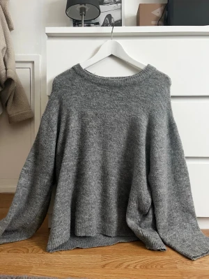 Grå oversized stickad tröja - Mysig grå stickad tröja med avslappnad, oversized passform och rund halsringning. Tröjan har långa ärmar och ribbade muddar vid ärmslut och nederkant. Perfekt för lager på lager och en chill look.