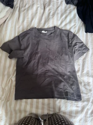 Grå basic t-shirt från Gina Tricot - En enkel och stilren grå t-shirt från Gina Tricot. Modellen är rak med korta ärmar och rund halsringning. Perfekt till jeans eller kjol och lätt att matcha med andra plagg. Tillverkad i mjuk bomull för skön känsla.