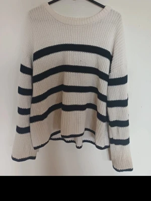 Randig stickad tröja från Selected Femme - Snygg stickad tröja från Selected Femme i vitt med svarta horisontella ränder. Tröjan har rund halsringning, långa ärmar och en avslappnad passform. Perfekt för en chill och trendig look.