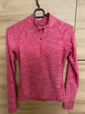 Rosa träningströja med halv dragkedja - Snygg rosa långärmad träningströja med melerad effekt och halv dragkedja framtill. Tröjan har hög krage och är tillverkad i ett stretchigt funktionsmaterial som passar perfekt till löpning eller gym. Figurnära passform och raglanärmar för extra rörelsefrihet.