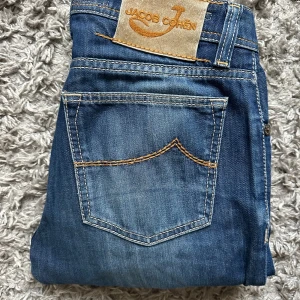 Blå Jacob Cohen jeans 688 - Snygga blå jeansbyxor från Jacob Cohen med klassisk femficksdesign, kontrastsömmar och raka ben. Jeansen har normal passform och är tillverkade i mjukt denimtyg med lätt tvättad look. Perfekta för en avslappnad och stilren outfit. Modell 688 (slim fit)