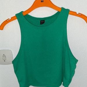 Grön croppad linnetopp från Shein - Snygg grön croppad linnetopp från Shein med rund halsringning och breda axelband. Toppen är ärmlös och har en enkel, stilren design i mjuk bomull. Perfekt för att skapa en fräsch och sportig look.