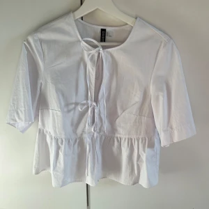 Vit blus med knyt och volang från Divided -  vit blus från Divided med knytning framtill och volang nertill. Blusen har korta ärmar💓💓endast använd en gång💗