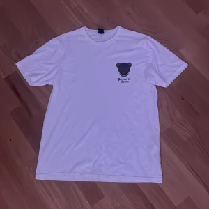 Vit t-shirt med björntryck - Vit t-shirt med korta ärmar och ett litet tryck av en björn samt texten 'Partner in Crime' på bröstet. Enkel och clean design som passar perfekt till jeans eller shorts. Skön passform och klassisk rund hals.