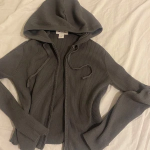 Grå ribbad kofta från Monki - Mysig grå kofta från Monki i ribbstickat material. Tröjan har dragkedja framtill, huva med snörning och långa ärmar. Perfekt för lager-på-lager och chill dagar. Enkel och stilren design som funkar till det mesta. Storlek XXS men passar upp till M