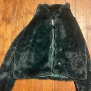Mörkgrön pälsjacka från Saint Tropez XS - Säljer en fluffig och mjuk mörkgrön pälsjacka från Saint Tropez i storlek XS. Jackan har en klassisk krage, dold knäppning och är helfodrad med glansigt tyg. Perfekt för dig som vill ha en trendig och mysig look under kyliga dagar.