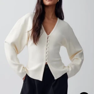 Beige kofta med v-ringning från Gina Tricot - Snygg beige kofta från Gina Tricot med v-ringad hals och dekorativa knappar framtill. Modellen är lite loose och har långa ärmar. Materialet är mjukt och stickat, perfekt för lager på lager. Enkel och clean design som är lätt att matcha.