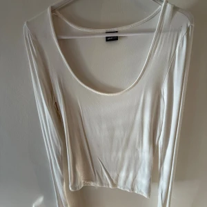 Vit långärmad topp från Gina Tricot - En stilren vit långärmad topp från Gina Tricot med rund, djup urringning. Tunn och mjuk i materialet, perfekt att styla med jeans eller kjol. Enkel och clean design som funkar till många looks.