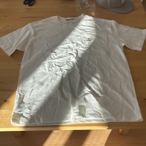 Vit Moncler t-shirt med logga - Vit t-shirt från Moncler med klassisk rund hals och broderad logga på bröstet. Säljer pågrund av att den är för stor. Skick 10/10 och helt ny