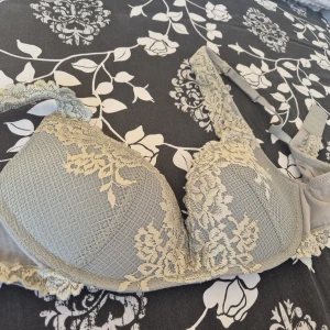 Grå spets-bh med blommönster - Säljer en snygg grå bh med vacker spets och blommiga detaljer. Bh:n har vadderade kupor och justerbara axelband. Perfekt för dig som gillar romantiska och feminina detaljer i din underklädesgarderob.