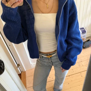 Blå stickad kofta från Envii - Säljer en blå stickad kofta från Envii. Koftan har lång ärm, ribbad struktur och dragkedja framtill. Perfekt att slänga över en topp för en chill och snygg look. Färgen är en djup blå och passformen är lite loose.