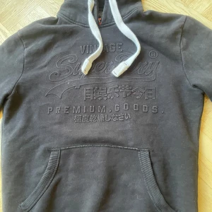 Svart Suprdry hoodie - Säljer denhär svarta hoodien från superdry. Den är i mycket bra skick förutom ett litet hål på ryggen.