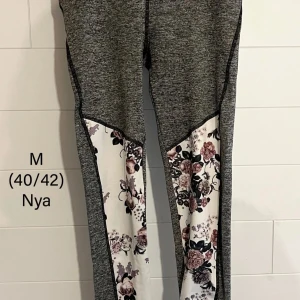 Grå leggings med blommiga detaljer - Snygga grå leggings med blommiga paneler i vitt, rosa och svart längs benen. Perfekta för träning eller chill, med bekväm passform och stretchigt material. Blommönstret ger en unik och trendig look.
