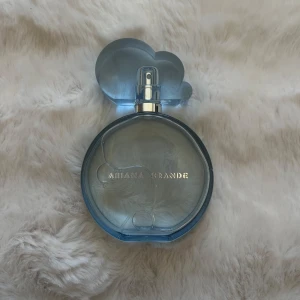 Ariana Grande blå parfymflaska - Trendig parfym från Ariana Grande i en snygg blå flaska med molnformad kork. Perfekt för dig som vill ha en cool accessoar på sminkbordet och gillar Ariana Grande.