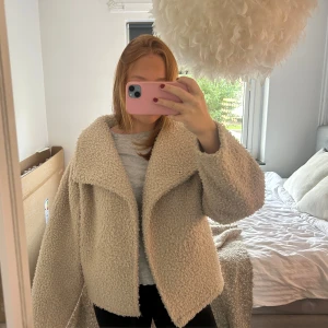 Beige teddyjacka med oversized krage - Säljer en beige teddyjacka med stor, bred krage och avslappnad passform. Jackan är fluffig och mjuk med ett stilrent uttryck, perfekt för dig som gillar en cozy vibe. Stängs med knapp framtill och har långa ärmar. Det är en stolek S men modellen gör så det känns som en S-M.