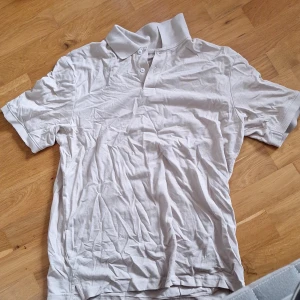 Vit pikétröja från H&M, storlek S - Klassisk vit pikétröja från H&M i storlek S. Tröjan har korta ärmar, krage och knäppning med två knappar framtill. Tillverkad i mjuk bomull som är skön mot huden. Perfekt för en clean och enkel stil.