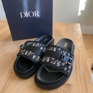 Svarta Dior tofflor med monogram - Säljer ett par Dior tofflor med det ikoniska dior monogrammet i storlek 42. De är helt nya och oanvända, kommer med box Vid fler frågor eller funderingar skicka ett pm, Mvh