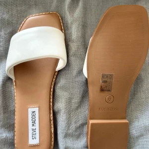 Vita sandaler Steve Madden - Snygga vita sandaler med bred rem över foten och fyrkantig tå från Steve Madden. Sulan är beige och har dekorativ söm runt kanten. Perfekta för en clean look till din outfit.