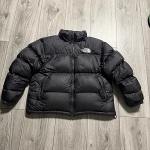 The North Face 1996 Retro Nuptse Men XL - Säljer en svart pufferjacka från The North Face i storlek XL. Jackan är dunfylld (700 fill power), har hög krage, dragkedja framtill och två sidofickor med dragkedja. Klassisk logga på bröstet och ärmen. Perfekt för kalla dagar.