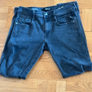 Svarta Replay Anbass jeans, stl 30/30 NYTT SKICK - Säljer ett par svarta Replay Anbass jeans i storlek 30. Jeansen har klassisk femficksdesign, smal passform och är tillverkade i stretchigt denim för extra komfort. Snygga detaljer och diskret Replay-logga på fickan.