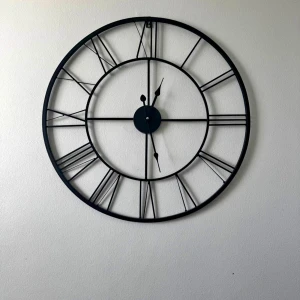 Mio Stor svart väggklocka i metall - Säljer en stor och stilren väggklocka i svart metall med öppet skelett-design och romerska siffror 45cm diameter. Perfekt som statement piece till rummet, klockan har tunna linjer och en rund form som ger en modern vibe.