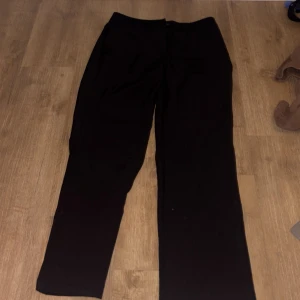 Svarta kostymbyxor från ONLY, stl 40 - Svarta kostymbyxor från ONLY tailoring i klassisk rak modell. Byxorna har knapp och dragkedja framtill och är perfekta för en clean och stilren look. Materialet känns mjukt och följsamt, vilket gör dem bekväma att bära hela dagen.