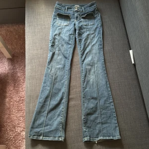 Blå bootcut jeans från Nelly - Snygga blå jeans från Nelly med bootcut-modell och två fickor fram till med en öppning(dom ligger inte helt rakt men det kan man fixa bara genom att stryka). Jeansen har dubbla knappar i midjan, tyvärr har dom lite slitningar ner till fötterna då dom har varot lite långa.