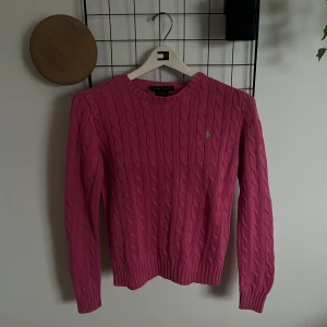 Rosa kabelstickad tröja från Ralph Lauren - Kabelstickad rosa tröja från Ralph Lauren i 100% bomull. Klassisk modell med rund halsringning, lång ärm och broderad logga på bröstet. Tråd har brytits lite i högra ärmen och lappen där bak har lossnat på ena sidan, annars fin. Lägg gärna prisförslag!