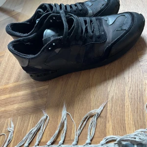 Valentino Rockrunner svarta sneakers - Säljer ett par svarta Valentino Rockrunner sneakers med coola camouflagedetaljer och nitar på hälen. Skorna är i en mix av skinn, mocka och textil, med snörning och platt sula. 